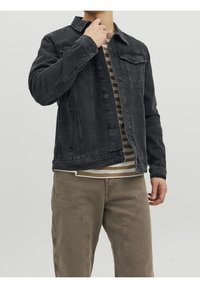 Black denim jacket with a button-up front, two chest pockets, and long sleeves, paired with a striped shirt and beige pants.