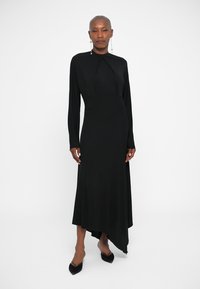 Sort langærmet kjole med en asymmetrisk kant, lavet af glat stof. Har en høj halsudskæring og et minimalistisk design med elegante linjer.