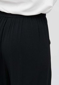 Zwarte tapered broek met een elastische tailleband. Gemaakt van zachte stof, met subtiele plooien voor extra textuur. Ideaal voor casual wear.