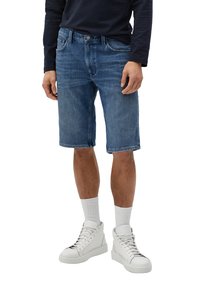 Denim-Shorts in mittlerem Blau, lockere Passform, knielang, mit Fünf-Taschen-Design und dezentem Verblassen. Kombiniert mit weißen Sneakers und gerippten Socken.