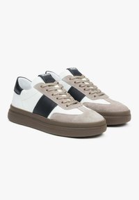 Sneakers wykonane z zamszu i skóry w odcieniach beżu, czerni i bieli. Mają zaokrąglony kształt, sznurowadła oraz teksturowane podeszwę.