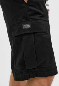 Czarne bawełniane szorty z boczną kieszenią, z etykietą z napisem "JACK & JONES". Materiał ma gładką fakturę i solidną konstrukcję.