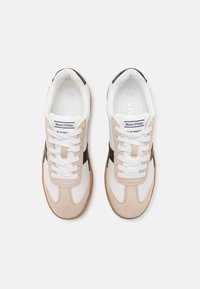 Ljusbeige och vita sneakers med svarta accenter. Tillverkade av mocka och mesh-material, rund tå, platt sula och vita snören. Logotyp på tungan.