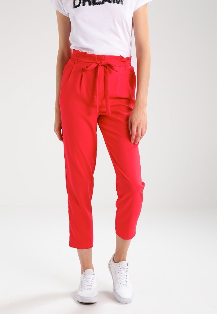Pantalon rouge taille haute avec ceinture à nouer, présentant une coupe droite, une texture lisse et une longueur raccourcie, assorti à des baskets blanches.