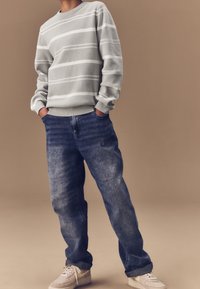 Pull en rayures gris clair avec un col rond, associé à un jean en denim bleu ample et des baskets beiges avec un swoosh blanc.