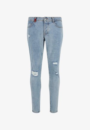 Heledad sinises teksaste püksid, millel on kitsas lõige, mitmed kulumisjäljed ja rebenditega servad. Esiküljel on tavaline nupukinnitusega sulgemine.