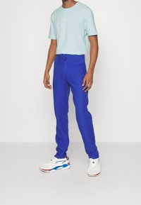 Blå linnekjol med dragsko i midjan, ihop med en ljusgrön bomullströja med en liten logotyp, och vita sneakers med färgglada detaljer.