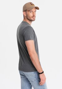 Camiseta gris de manga corta hecha de tela suave, combinada con jeans de color azul claro. La persona lleva una gorra color tostado con acentos bordados.