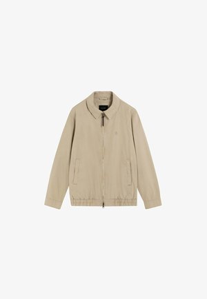 Chaqueta ligera beige con cremallera frontal, dos bolsillos laterales, dobladillo elástico y cuello clásico, extendida sobre fondo blanco.