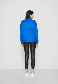 Blå strikket genser med høy hals, kombinert med svarte leggings og hvite joggesko. Genseren har droppede skuldre og en avslappet passform.