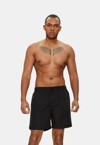 Pantaloni da bagno neri con cintura elastica e cordino. Il modello è senza camicia, mostrando un grande tatuaggio a forma di ala sul petto.