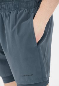 Donkergrijze sportshorts van lichtgewicht stof. Voorzien van een elastische tailleband, zijzakken en een logo "ENDURANCE" nabij de zoom.