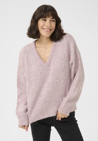 Pulover tricotat, roz deschis, cu decolteu în V, umeri lăsați și manșete cu nervuri. Textură moale și croială ușor lejeră pentru confort.