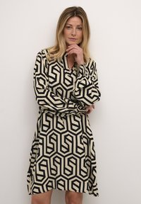 Vestido de patrón geométrico en blanco y negro con escote en V, mangas largas y puños fruncidos, hecho de una tela suave y ligera.