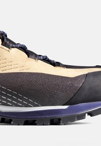 Scarpa da trekking con tomaia marrone chiaro e nera, caratterizzata da materiali strutturati, puntale sagomato e suola robusta viola con battistrada antiscivolo.