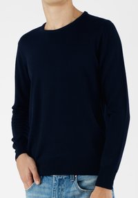 Maglione blu navy a girocollo realizzato in tessuto morbido, con polsini e bordo a costine. Indossato sopra jeans azzurri, con una vestibilità casual.