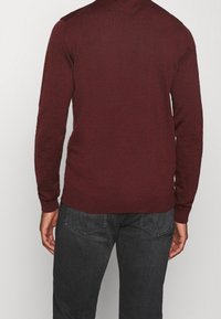 Bordeauxfarbener Pullover mit langen Ärmeln und gerippten Bündchen. Hergestellt aus strukturiertem Strickgewebe mit engem Schnitt und nahtlosen Schulterakzenten.