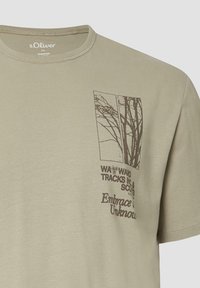 Beige s.Oliver T-shirt met een grafiek van boomtakken en de tekst "WAYWARD TRACKS INC. & SCOUTS" en "Omarm het Onbekende" op de borst.