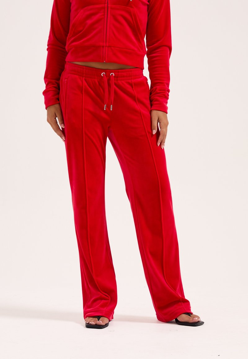 Tuta in velluto rosso con giacca corta con zip e pantaloni larghi, dotati di vita con coulisse e tasche laterali. Tessuto morbido.
