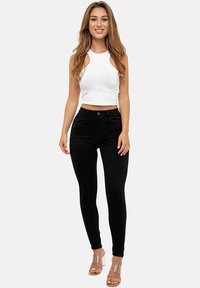 Jeans skinny negros de talle alto con cuatro bolsillos. Combinados con una camiseta sin mangas blanca y corta. Sandalias de tacón alto transparentes completan el conjunto.