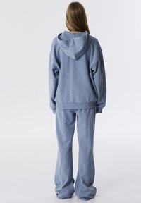 Felpa blu chiaro e pantaloni coordinati realizzati in morbido tessuto, con accenti decorativi di borchie lungo i lati dei pantaloni.