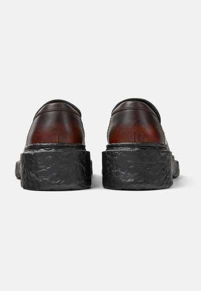 Scarpe in pelle marrone scuro con suole platform nere spesse e strutturate, viste da dietro su sfondo bianco.