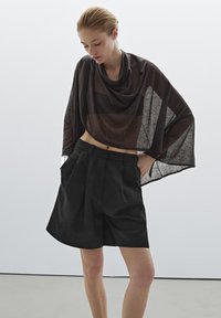 Pantaloni corti neri su misura con plisse, abbinati a una blusa trasparente marrone, drappeggiata, caratterizzata da una vestibilità ampia e una varietà di opacità.