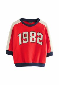 Sweatshirt rouge à coupe loose, avec des accents blancs et bleu marine, "1982" imprimé en blanc, poignets et ourlet côtelés.