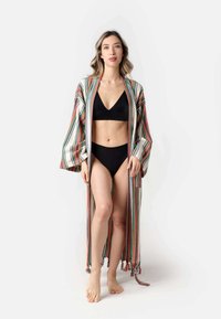 Robe stile kimono a righe con vivaci strisce multicolore, apertura frontale, maniche lunghe e dettagli con pon-pon lungo l'orlo, indossato sopra un bikini nero.