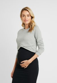 Sweatshirt cinza, cropped, com mangas longas, feito de material suave, combinado com uma saia preta justa. Design simples e clean.