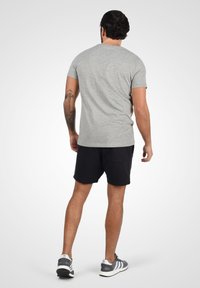 Camiseta de hombre gris de manga corta, combinada con pantalones cortos negros. Presenta un cuello redondo y una textura de tela suave, utilizada con zapatillas deportivas grises.