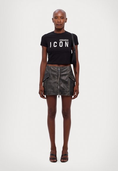 Black cropped t-shirt with “ICON” print, paired with a gray leather mini skirt featuring a front zipper and side pockets. Black sandals.