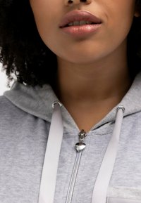 Grau zip-up Kapuzenpullover mit einem silbernen herzförmigen Zipper und passenden Kordeln. Die weiche Textur und die lockere Passform betonen den Halsausschnitt.