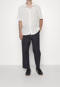 Camisa blanca de manga corta, con botones, y un patrón de textura de punto, combinada con pantalones holgados de color azul marino oscuro y zapatillas deportivas negras.