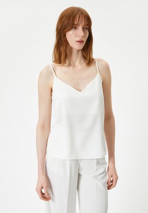 Camisón de satén blanco con tirantes finos y escote en V. Corte holgado con una textura suave, combinado con pantalones de color claro.