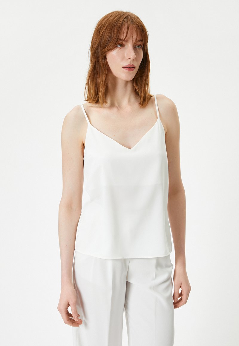 Witte satijnen camisole met dunne bandjes en een V-hals. Losse pasvorm met een gladde textuur, gecombineerd met lichtgekleurde broeken.