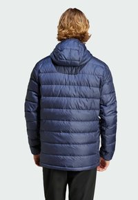 Marineblå puffjakke med hætte, med en quiltet design, glat tekstur og elastiske manchetter. Dækker taljen, mellemlang stil.