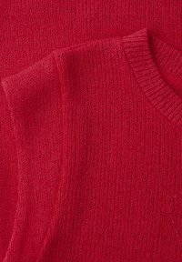 Due maglioni rossi lavorati a maglia sovrapposti, con dettagli di trama e scollo rotondo a coste sul maglione superiore.