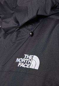 Primer plano de tela de chaqueta negra con el logo "The North Face" bordado en blanco y un cierre de cordón negro en la capucha.