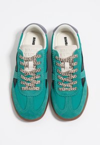 Zapatillas de ante azul verdoso con cordones beige y detalles en negro. Presentan una puntera redondeada y una suela de goma texturizada. Logo en la lengüeta.