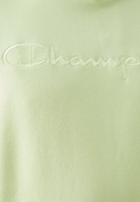 Felpa verde chiaro realizzata in tessuto morbido, presenta un logo "Champion" ricamato in un colore abbinate. Design semplice con scollatura rotonda.