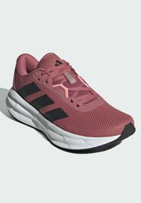 Pink mesh sneaker with black stripes, white midsole, and textured accents. Features a rounded toe and lace-up design for secure fit.