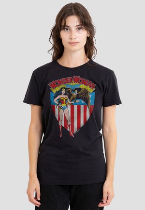 Young woman with brown hair wearing a black Wonder Woman t-shirt featuring the character and an eagle over red, white, and blue shield.