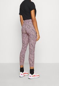 Legginsy w panterkę w różowym i czarnym kolorze z wysokim stanem, w połączeniu z czarną koszulką z krótkim rękawem i białymi trampkami.