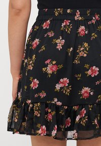 Svart blomsterkjole med rosa blomster og grønne blader. Elastisk linning og volangkant. Lett stoff med en gjennomsiktig overlag.