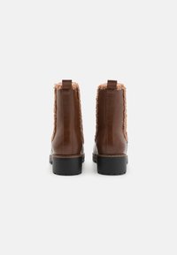 Bottines en cuir marron avec une bordure en fausse fourrure, bout arrondi et semelle en caoutchouc noir texturé. Équipées de tirettes pour un enfilage facile.