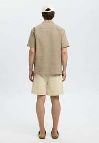 Korte mouw beige textuurshirt, kaki shorts en sandalen. Het shirt heeft een subtiel quiltpatroon en een standaard kraag.