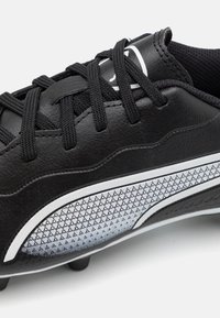 Botas de fútbol sintéticas negras con parte superior texturizada, franjas blancas de acento y un lateral con un patrón. Cordones y tacos moldeados visibles.