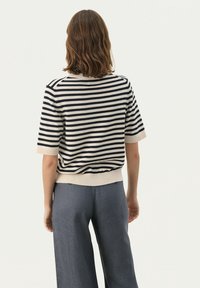 Striped short-sleeve knit sweater in cream and navy, featuring a ribbed neckline and hem. Paired with wide-leg gray pants.