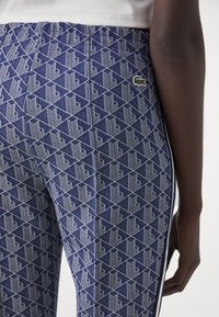 Navy patterned leggings featuring a geometric design with white accents, elastic waistband, and a small green logo patch on the side.